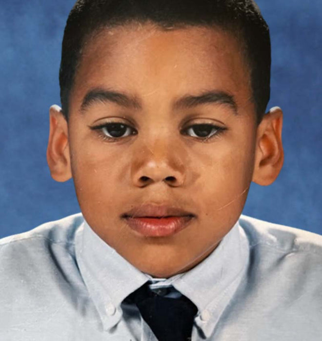 Young boy in a light blue shirt and dark tie, posing against a blue background.