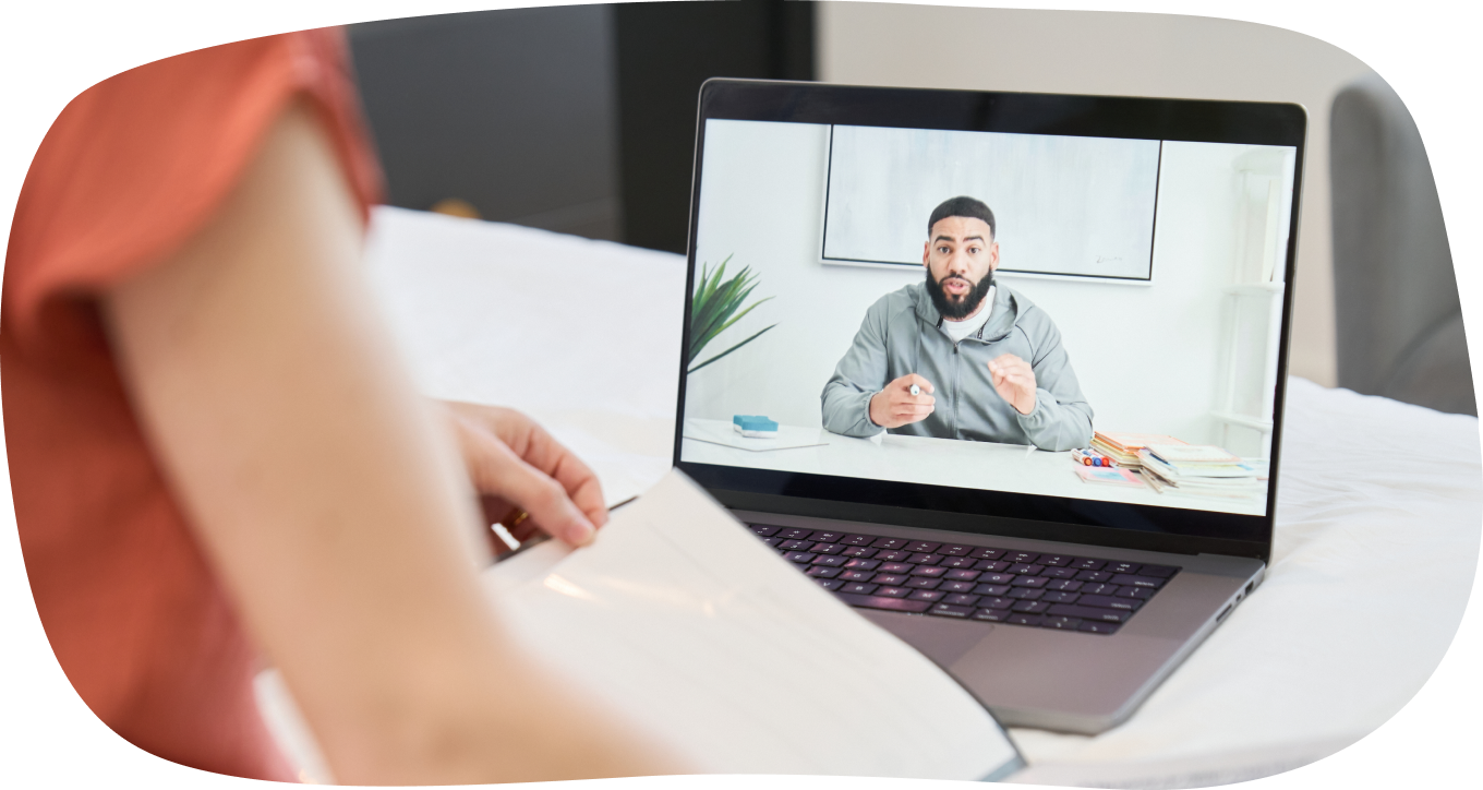 Person watching an online lecture on a laptop, showing a man speaking in front of a whiteboard.